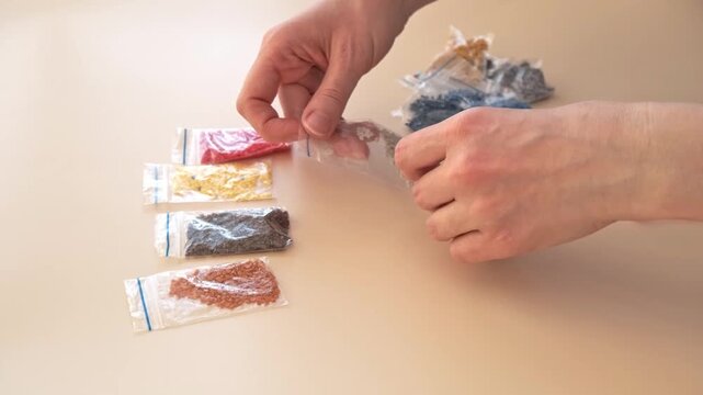 A woman rearranges small transparent bags with a diamond mosaic on a smooth, light-colored surface, side view, hands close-up.