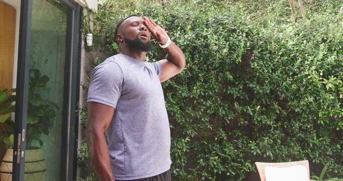 African adult male feeling overheated on sunny patio, holding green water bottle, pressing forehead