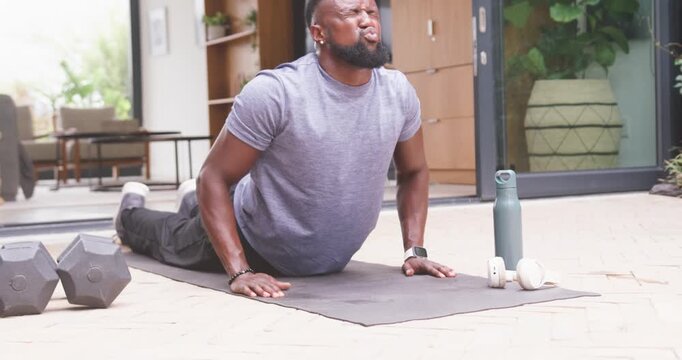 Man exercising in workout clothes, pushing from prone to extended back on patio mat with weights