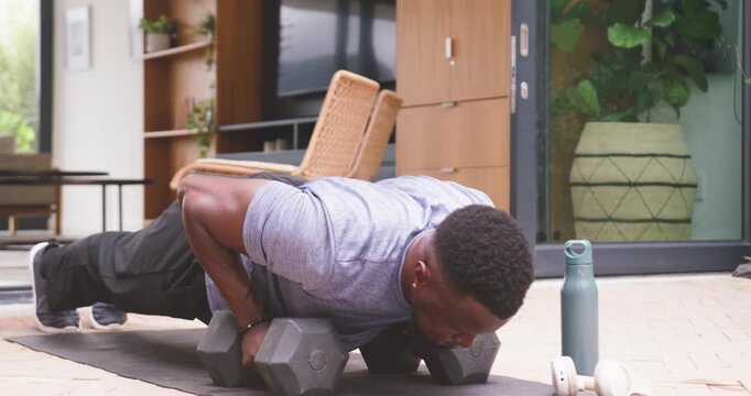 African American man in gray tee gripping hex weights lowering chest pressing at patio for strength