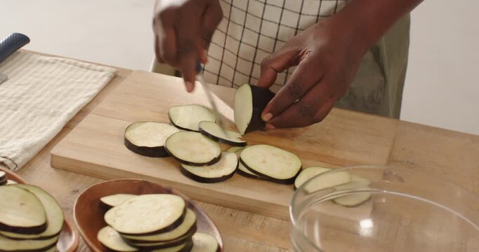 African man holding eggplant, slicing, stacking and dicing with knife on cutting board for cooking