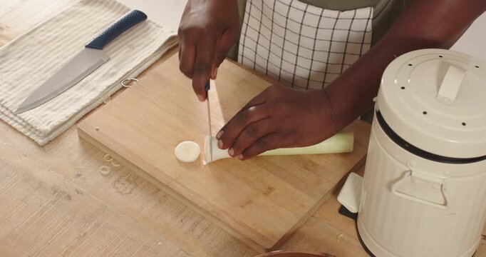 Chef's knife is slicing white-and-light-green leek into thin rounds on wooden cutting board