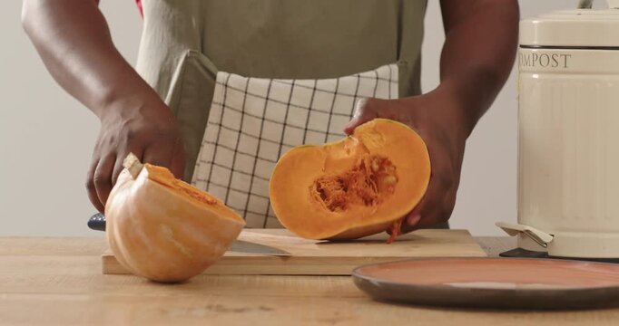 African man cutting squash with chef knife on board in kitchen wearing olive apron COMPOST