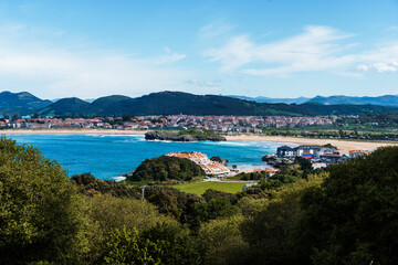 Fototapeta premium Scenic coastal view of Isla, Cantabria, featuring a town, beach, and sea under a blue sky.
