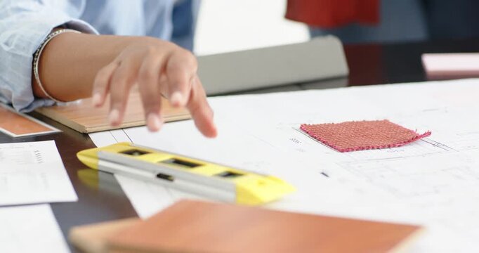 Diverse female coworkers reviewing in studio, one woman sliding level across plans near red swatch