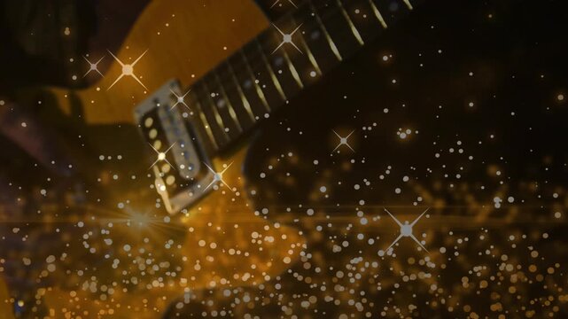 Plucking gold electric guitar, hands in dark sleeves moving on fretboard in dim studio, star bokeh
