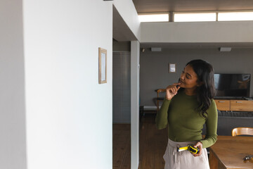 Woman holding tape measure and pencil measuring picture placement on white wall at home, copy space