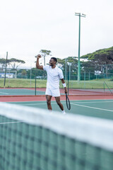 Obraz premium African American male celebrating holding tennis racket while wearing all white on hard court