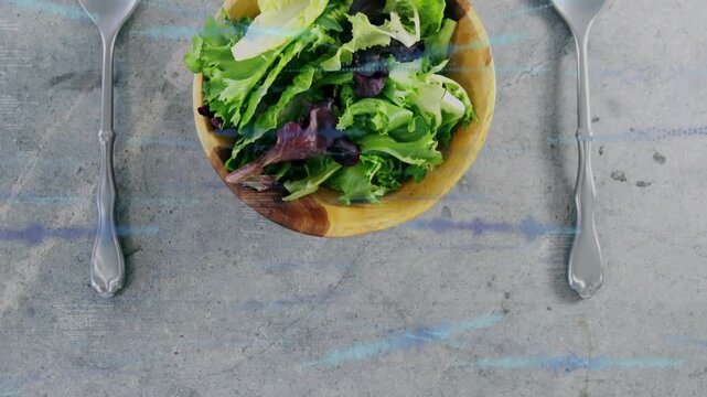 Vertical video: Placing wood bowl with greens on concrete to serve spoon and fork, blue streaks