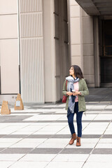 Mature woman standing in plaza wearing parka holding coffee cup carrying red bag and looking left © wavebreak3