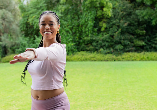 Mid-adult African-American woman reaching arm on lawn, wearing pink set, tracker, hoops, copy space