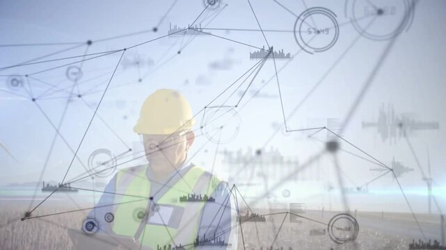 Field engineer tapping tablet in windfarm, animated network orbiting him monitoring turbines