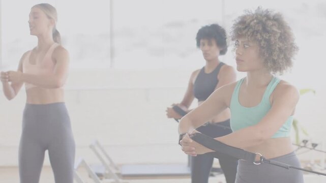 Holding center woman in mint top dark leggings mirroring coach cues at studio holding straps, watch