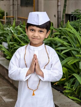 Cute Indian boy in traditional Marathi attire with Gandhi cap and tulsi mala greeting with namaste, representing Warkari culture and Palkhi festival in a peaceful outdoor setting.