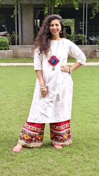Indian woman in casual ethnic kurta with colorful embroidered palazzo pants, posing outdoors on grass, showcasing modern fusion fashion with traditional touch.