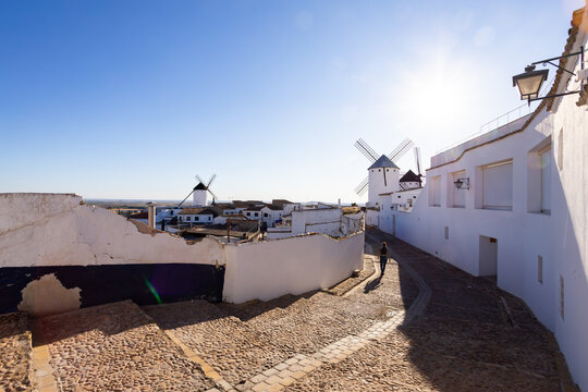 Person walking on cobbled street with windmills in Campo de Criptana