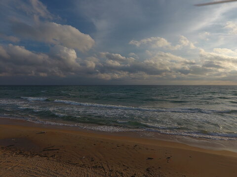Ocean waves gently rolling onto sandy beach under cloudy sky at day