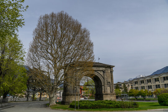 Arch of Augustus, ancient Roman triumphal arch framed by a large bare tree, Aosta, Italy
