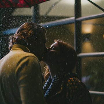 A boyfriend and girlfriend is kissing one another in the rain