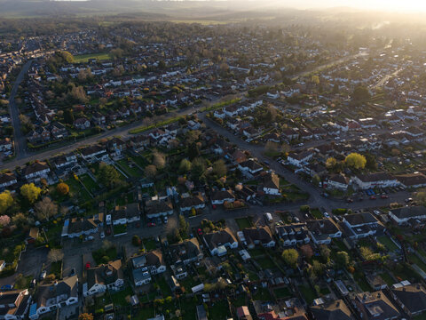 Sunrise above above the town with hundreds of houses. High altitude aerial view of urban landscape with straight road leading towards the sun. Side streets with residential houses and gardens.