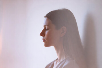 Fototapeta premium Subject: A woman with her eyes closed. Action: Contemplation or meditation. Setting: An indoor, softly lit space with a textured background.