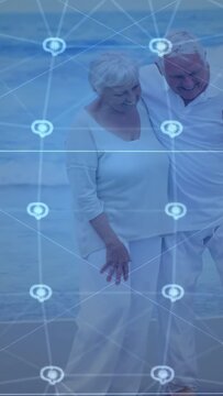 Walking senior couple arm-in-arm on beach in light tops holding yellow dog leash under blue overlay