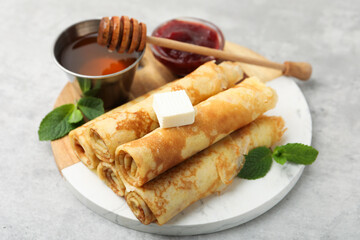 Tasty rolled crepes with honey, jam, butter and mint leaves served on light grey table, closeup © New Africa