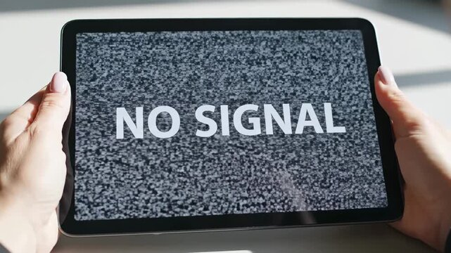 This shows a person holding a tablet with a snowy screen displaying a no signal error message, indicating technical difficulties or loss of connectivity.