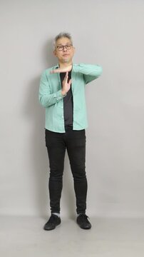Mature Asian man making a "T" timeout hand gesture to signal a break or stop in vertical 4K studio video.