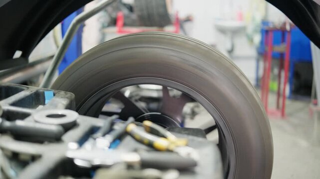 Car wheel spinning on a balancing machine in a professional auto service workshop. Mechanic checking the tire rotation to ensure proper vehicle alignment and performance on the road