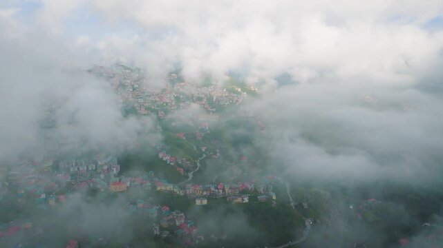 Cinematic drone flight through low clouds revealing the densely packed mountain city of Shimla, India.