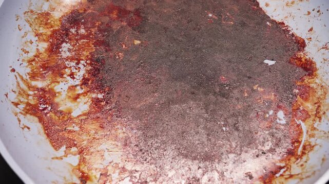 A close-up of a dirty pan with burnt food residue. The shot represents kitchen mess, cooking mistakes, and household cleaning concept.