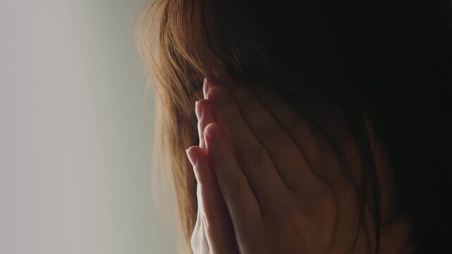 A close up of a tired and upset woman rubbing her face and eyes. She covers her face with her hands as she tries to relax and cope with stress.