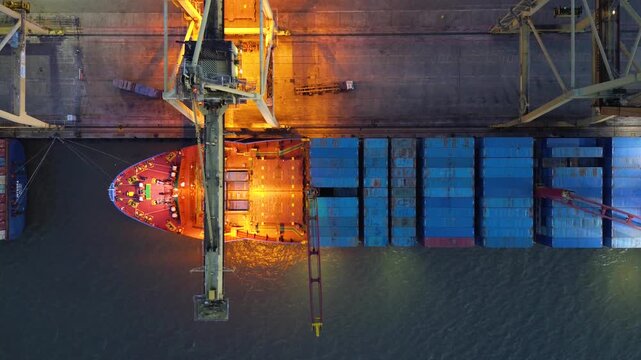 Container crane loading cargo ship at a busy port terminal at night with illuminated industrial activity