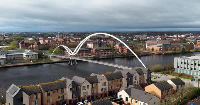 Aerial view of town of Middlesbrough showing the Infinity Bridge crossing the River Tees with modern buildings riverside housing captured from above in spring time with clear detail and calm water