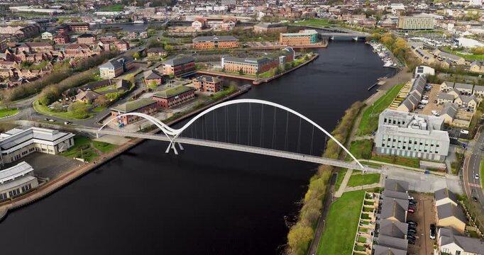 Aerial view of town of Middlesbrough showing the Infinity Bridge crossing the River Tees with modern buildings riverside housing captured from above in spring time with clear detail and calm water