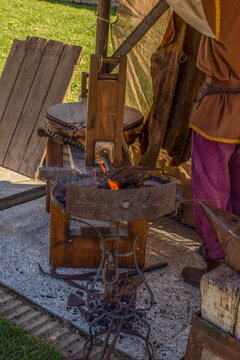 Close up of a traditional medieval forge with glowing fire, wooden bellows, and a blacksmith in period costume. Ideal for historical reenactment, ancient craftsmanship, and heritage themes.