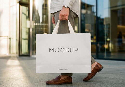 White Paper Shopping Bag Mockup Held by a Man Walking On City Street, Minimalist Blank Template for Branding