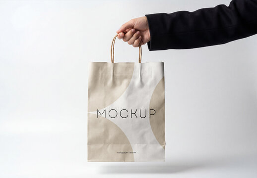 Hand Holding A White Paper Shopping Bag Mockup Against A Plain White Background, Isolated Blank Packaging Template