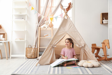Little girl drawing in sketchbook near toy wigwam at home, space for text © New Africa