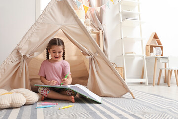 Little girl drawing in sketchbook near toy wigwam at home, space for text © New Africa