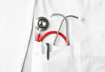 Fototapeta premium Stethoscope and pens in pocket of white doctor’s coat on light background, top view