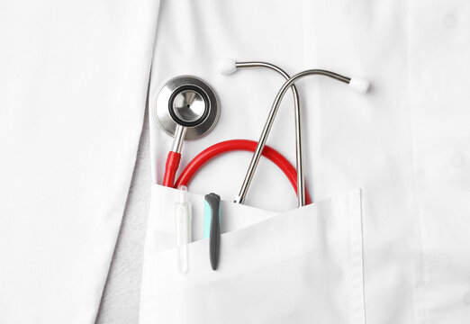 Stethoscope and pens in pocket of white doctor&rsquo;s coat on light background, top view