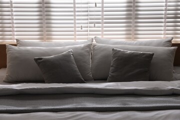 Large bed with pillows and blanket near window in room