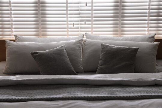 Large bed with pillows and blanket near window in room