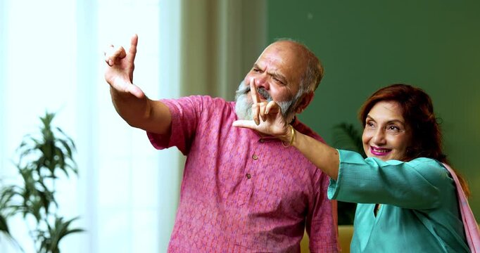 An Indian senior couple standing together and using one hand each to create a rectangular frame gesture. They are visualizing their future home and planning a creative project in the living room