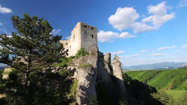 Lietava castle in Slovakia, Europe. Rugged castle ruins overlook vibrant green valleys. Ancient stone castle perched on steep cliff. Green forests and rolling hills below. Bright blue sky