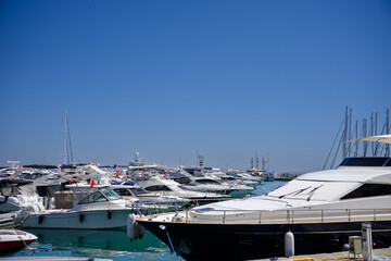 Fototapeta premium Luxury yachts, sailboats moored at sunny Mediterranean marina. Nautical lifestyle, high-end travel and summer vacation concept, marine transportation. Marina harbor with turquoise water under sky