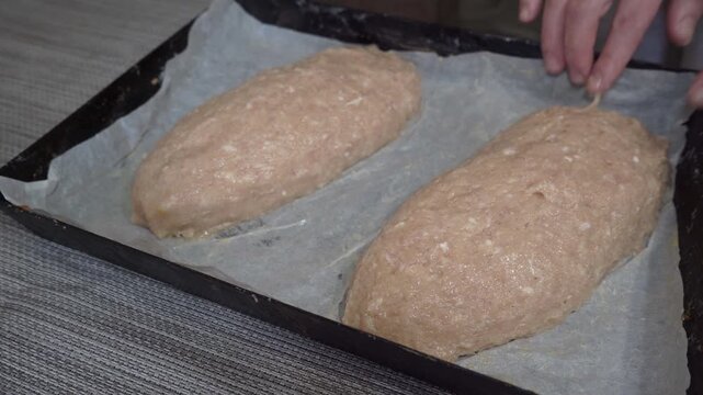 Shaping homemade meatloaf Hare.The process of making meatloaf at home. The cook forms two oblong loaves of minced meat on a black baking sheet.