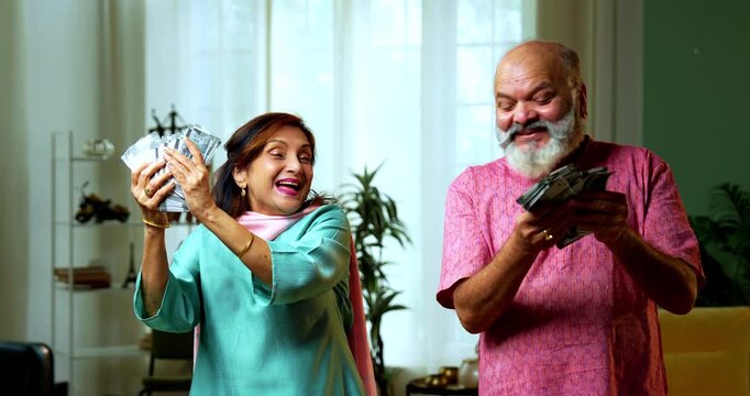 An Indian senior couple standing together holding a large stack of five hundred rupee notes. They are overwhelmed with joy and cheering over their financial savings and wealth at home